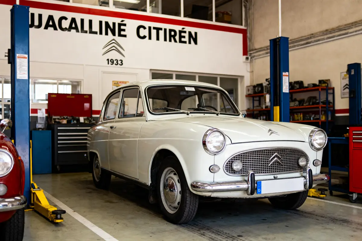 Voiture vintage Citroën blanche dans un garage, avec équipement de réparation et logo Citroën visible.