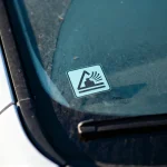 Autocollant sur vitre d'une voiture, indiquant un danger de chute de pierres.