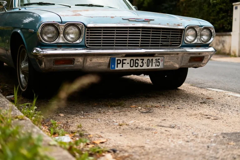 Voiture classique bleu avec plaque d'immatriculation française, garée sur un chemin en gravier, entourée de verdure.