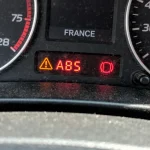 Voyant d'alerte ABS allumé sur tableau de bord de voiture, fond noir.