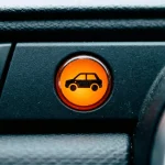 Voyant lumineux orange avec icône de voiture dans un tableau de bord noir.
