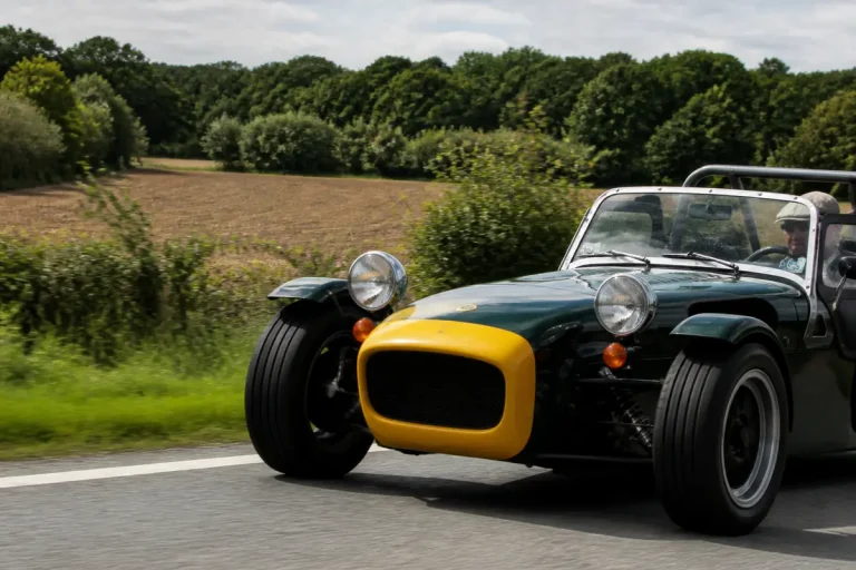 Voiture de sport verte et jaune roulant sur une route de campagne, entourée d'arbres.