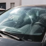 Parbrise de voiture fissuré par impact circulaire, dans un environnement urbain.