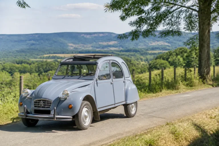 Voiture ancienne Citroën grise sur route de campagne verdoyante avec montagne en arrière-plan