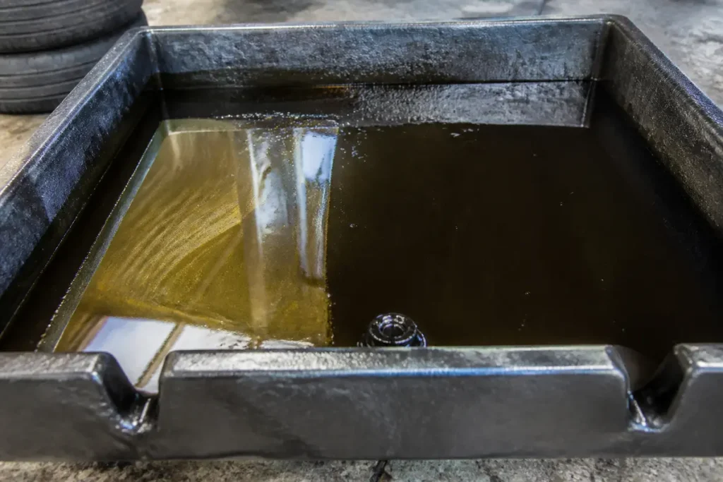 Bac contenant liquide sombre illustrant la couleur de l'huile moteur usagée dans garage