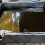 Bac contenant liquide sombre illustrant la couleur de l'huile moteur usagée dans garage