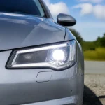 Vue rapprochée d'une voiture grise avec feux avant allumés sur route ensoleillée