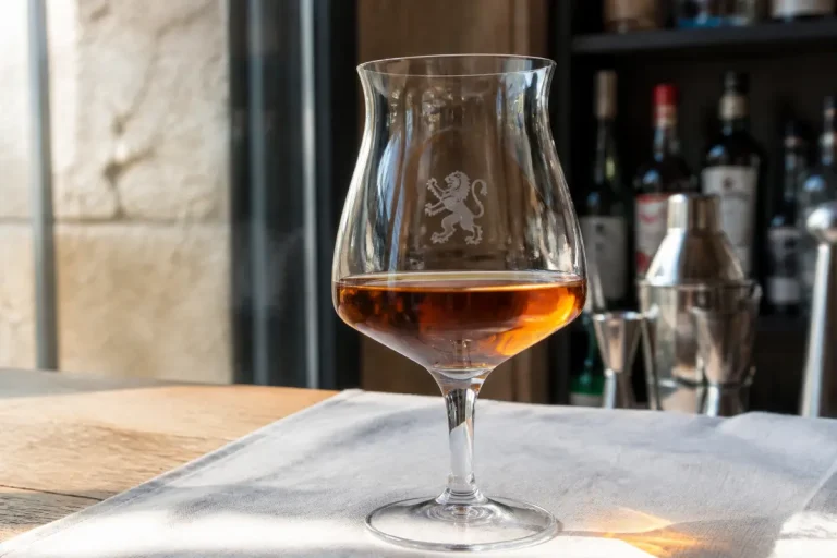 Verre Peugeot avec logo gravé et boisson ambrée sur table en bois d'un bar
