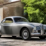 Voiture des années 1950 grise garée devant une maison avec arbres en arrière-plan